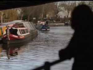 A figure stands in shadow, looking out over a canal